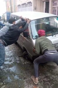 जालौन के कोंच में खुले सीवर चेंबर में फंसी स्कूली बच्चों की वैन और मदद करते स्थानीय लोग।