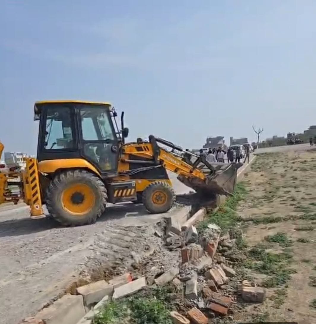 उरई के झांसी रोड पर अवैध प्लॉटिंग को ध्वस्त करता विकास प्राधिकरण का बुलडोजर और मौके पर उपस्थित पुलिस बल एवं अधिकारी