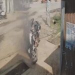 जालौन के एट कोतवाली क्षेत्र में हाईटेंशन तार गिरने से धू-धू कर जलती हुई मोटरसाइकिल और आसपास जमा भीड़