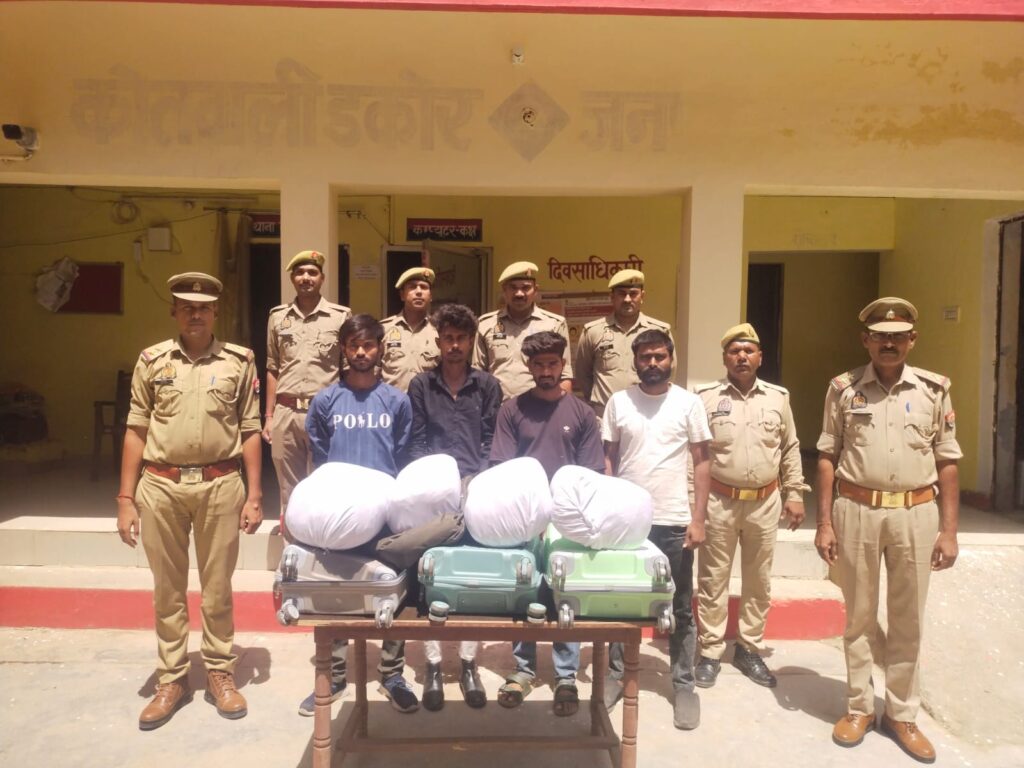 जालौन में पुलिस का बड़ा एक्शन: अंतर्जनपदीय गांजा तस्करी गिरोह का भंडाफोड़, 24 किलो से अधिक अवैध गांजे के साथ 4 तस्कर गिरफ्तार news image जालौन पुलिस की गिरफ्त में खड़े चार गांजा तस्कर, मेज पर बरामद 24 किलो अवैध गांजा, तीन ट्रॉली बैग और मोबाइल फोन रखे हुए।