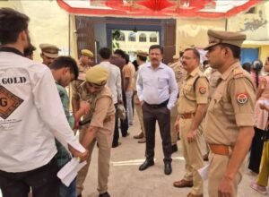 उत्तर प्रदेश पुलिस भर्ती परीक्षा 2026 के दौरान जालौन के एक परीक्षा केंद्र पर अभ्यर्थियों का बायोमेट्रिक सत्यापन और सघन तलाशी लेते सुरक्षाकर्मी, पृष्ठभूमि में निरीक्षण करते जिलाधिकारी और पुलिस अधीक्षक।