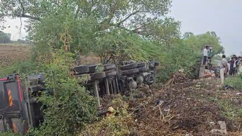 जालौन-कोंच मार्ग पर उदोतपुरा गांव के पास गिट्टी से भरा हुआ अनियंत्रित डम्पर सड़क किनारे खाई में पलटा हुआ, मौके पर बिखरी गिट्टी और जुटी ग्रामीणों की भीड़।