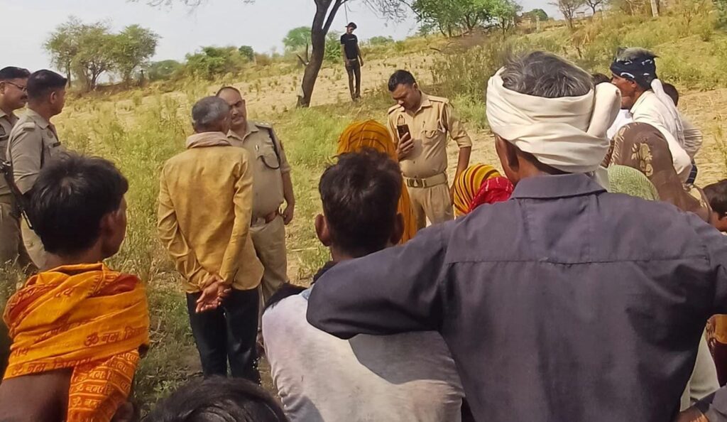 जालौन के कालपी कोतवाली क्षेत्र के रायड़ दिवारा गांव के बाहर एक पेड़ के पास खड़ी पुलिस और ग्रामीणों की भीड़, जहाँ 25 वर्षीय धर्मेंद्र का शव फंदे से लटकता हुआ मिला।