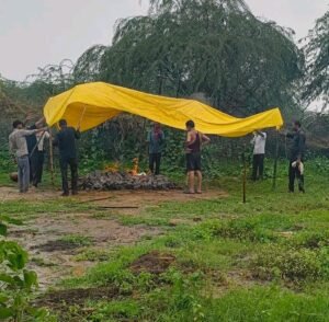 जालौन के नौरेजपुर गांव में बारिश के दौरान तिरपाल लगाकर किए जा रहे अंतिम संस्कार का दृश्य, मौजूद ग्रामीण और श्मशान घाट की व्यवस्था न होने की तस्वीर।