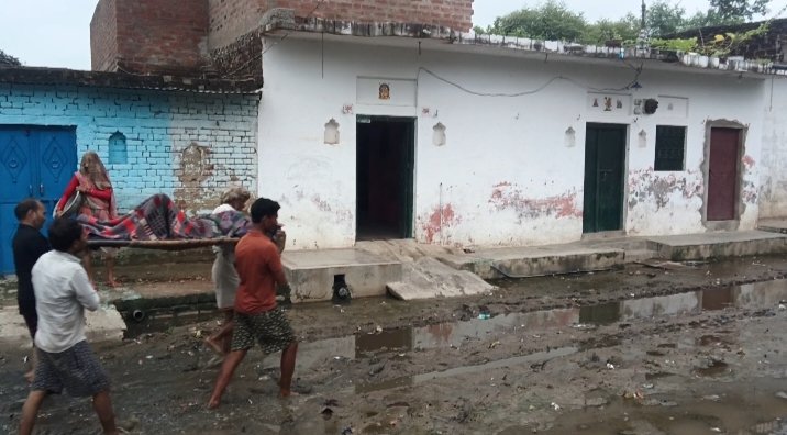 करमेर गांव में कीचड़ भरे रास्ते से चारपाई पर बीमार महिला को ले जाते ग्रामीण